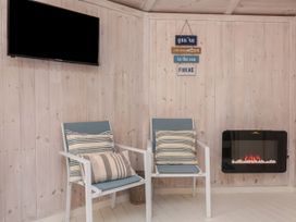 Two chairs with striped cushions a wall-mounted television a wall-mounted electric fireplace and wooden panel walls at Barley Bay near Hartland