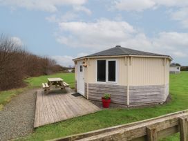 A small octagonal cabin with wooden siding and a picnic table on a wooden deck outside at Duck Pool near Hartland