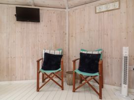 Two wooden chairs with cushions against wood-paneled walls with a wall-mounted TV and a tower fan at Duck Pool near Hartland
