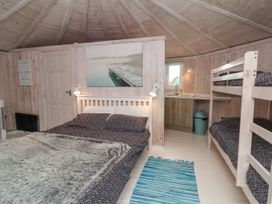 A bedroom with a double bed a bunk bed a small kitchen area and a striped rug at Duck Pool near Hartland
