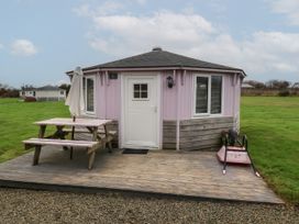 A round building with a white door and windows with blinds a wooden picnic table with an umbrella and a wheelbarrow on a wooden deck at Spekes Mill near Hartland