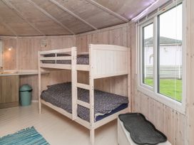 A room with a wooden bunk bed beside a window and a kitchenette with a trash bin at Spekes Mill near Hartland