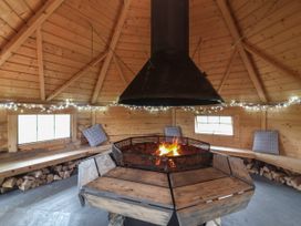 An octagonal wooden room with a central fire pit and a chimney hood surrounded by wooden benches with cushions and string lights near Hartland