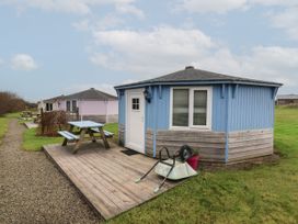 A blue wooden round cabin with a white door and window and a wooden picnic table on a deck near Hartland