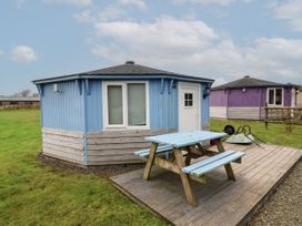 A blue round cabin with a wooden picnic table on a deck and a purple round cabin in the background at Widemouth Bay near Hartland