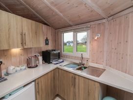 A kitchen with wooden cabinets a double sink an electric kettle and a window showing grass at Widemouth Bay near Hartland