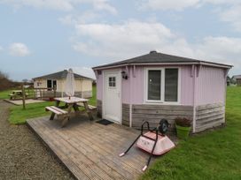 Two octagonal wooden cabins with outdoor picnic tables and an overturned wheelbarrow on a wooden deck at Widemouth Bay near Hartland