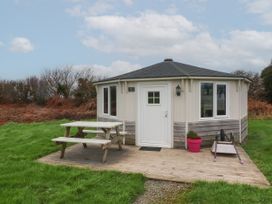 An octagonal cabin with a white door and windows on a wooden deck with a picnic table and a wheelbarrow on grass at Berry Bay near Hartland
