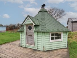 A small green BBQ hut with a wooden door and window on a wooden deck in a grassy area at Berry Bay near Hartland
