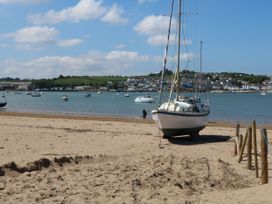 A sailboat on a sandy beach with several boats in the water and houses on a hillside at Berry Bay near Hartland