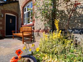 A wooden bench against a stone wall with a black door and window next to a garden with yellow and red flowers at 3 Railway Cottages in Long Marton near Appleby-In-Westmorland