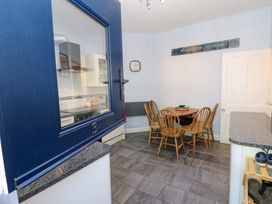 A kitchen dining area with wooden chairs and a table a blue door with number 3 and a clock on the wall at 3 Railway Cottages Long Marton near Appleby-In-Westmorland