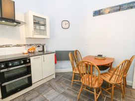 A kitchen with a stove, cabinets, a small wooden dining table, four wooden chairs, and a wall clock at 3 Railway Cottages in Long Marton near Appleby-In-Westmorland