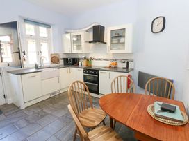 A kitchen with white cabinets wooden table and chairs tiled floor and a wall clock at 3 Railway Cottages in Long Marton near Appleby-In-Westmorland