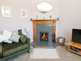 A living room with a green sofa and cushions a fireplace with a burning wood stove a TV on a wooden stand and a basket with gloves at 3 Railway Cottages in Long Marton near Appleby-In-Westmorland