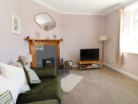 A living room with a green sofa, fireplace, television on a wooden stand, and a floor lamp at 3 Railway Cottages in Long Marton near Appleby-In-Westmorland