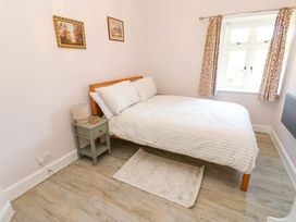 A bedroom with a double bed white bedding a bedside table with a lamp two paintings on the wall and a window with patterned curtains at 3 Railway Cottages Long Marton near Appleby-In-Westmorland