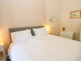 A bedroom with a large bed with white bedding and two bedside tables with lamps and a white dresser with a vase and wall mirror at 3 Railway Cottages in Long Marton near Appleby-In-Westmorland