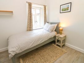 A small bedroom with a single bed striped bedding a nightstand with a lamp a window with patterned curtains and a framed painting on the wall at 3 Railway Cottages in Long Marton near Appleby-In-Westmorland