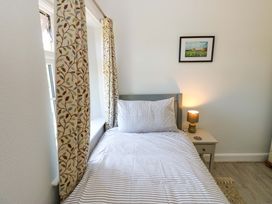 A single bed with striped bedding next to a window with patterned curtains and a nightstand with a lamp in a bedroom at 3 Railway Cottages in Long Marton near Appleby-In-Westmorland