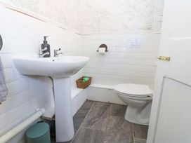 A bathroom with a pedestal sink soap dispenser toilet paper holder and a closed toilet seat at 3 Railway Cottages in Long Marton near Appleby-In-Westmorland