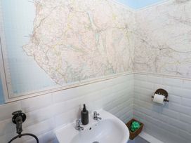 A bathroom corner with a sink, soap dispenser, toilet paper holder, map on the walls, and a basket with items at 3 Railway Cottages in Long Marton near Appleby-In-Westmorland