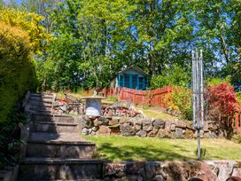 A garden with stone steps leading to a seating area with chairs and a table a shed and red wooden fence at 3 Railway Cottages Long Marton near Appleby-In-Westmorland