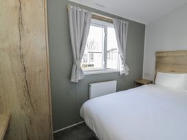 A bedroom with a bed, curtains, and a window at Lido Silver Plus 111 in Prestatyn