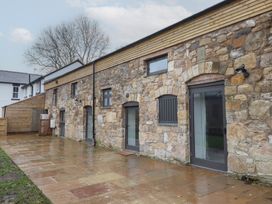 An outdoor stone patio area next to a stone building with several windows and doors at Sally's Barn in Weston Rhyn