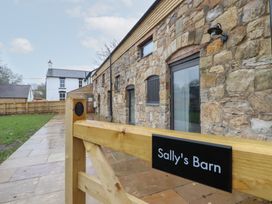 A stone barn building with a wooden gate labeled Sally's Barn and a paved walkway at Sally's Barn in Weston Rhyn