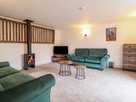 A living room with two green sofas a wood burning stove a television on a wooden stand two round wooden tables a wooden chest of drawers and a framed picture on the wall at Sally's Barn in Weston Rhyn