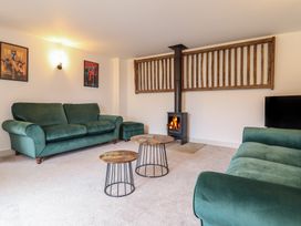 A living room with green sofas a wood stove two round wooden tables and framed pictures on the wall at Sally's Barn in Weston Rhyn
