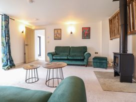 A living room with green sofas wooden coffee tables a wood stove and framed pictures on the wall at Sally's Barn in Weston Rhyn