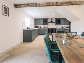 A kitchen with dark cabinets, a black oven, green upholstered chairs at a wooden dining table at Sally's Barn in Weston Rhyn