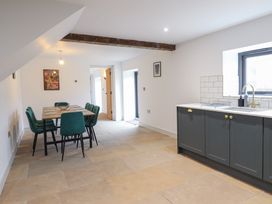 A dining area with a wooden table and green chairs next to a kitchen with gray cabinets and a window at Sally's Barn in Weston Rhyn