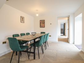 A dining room with a wooden table and eight green chairs and two framed pictures on the wall at Sally's Barn in Weston Rhyn