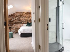A bedroom with a white bed and exposed brick wall next to a bathroom with a glass shower enclosure at Sally's Barn in Weston Rhyn