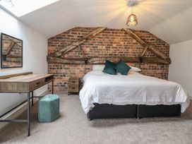 A bedroom with a brick accent wall wooden beams a bed with white bedding and green pillows a wooden desk and a green pouf at Sally's Barn in Weston Rhyn