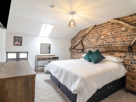 A bedroom with a bed white bedding wooden dresser small desk and exposed brick wall with wooden beams at Sally's Barn in Weston Rhyn