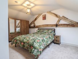 A bedroom with a double bed and floral bedding wooden wardrobe with mirrored doors and rustic wooden beams on walls at Sally's Barn in Weston Rhyn