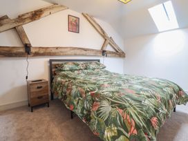 A bedroom with a bed covered by a tropical patterned duvet two wooden nightstands and exposed wooden beams on the wall at Sally's Barn in Weston Rhyn