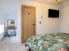 A bedroom with a wooden door a wall-mounted television and a dressing table with a mirror and ottoman at Sally's Barn in Weston Rhyn