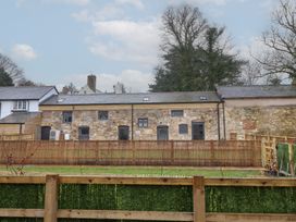 A stone building with several windows and doors behind a wooden fence and green hedge at Sally's Barn in Weston Rhyn
