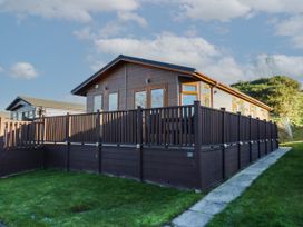 A brown wooden cabin with a fenced deck and grass surrounding it at The Sanctuary Badgers Retreat Holiday Park near Catterick Garrison North Yorkshire