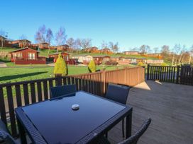 An outdoor patio with a glass table and chairs overlooking wooden lodges on grassy slopes at The Sanctuary Badgers Retreat Holiday Park near Catterick Garrison North Yorkshire