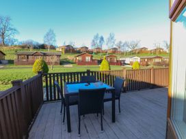 An outdoor deck with a table and four chairs overlooking multiple cabins on a grassy hillside at The Sanctuary Badgers Retreat Holiday Park near Catterick Garrison North Yorkshire