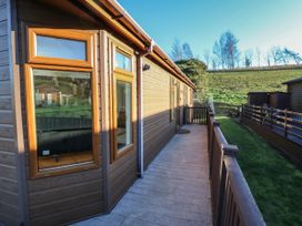 A wooden exterior of a lodge with windows and a deck walkway with railing overlooking a grassy hill at The Sanctuary in Badgers Retreat Holiday Park near Catterick Garrison North Yorkshire