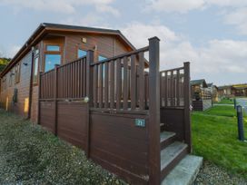 Exterior view of a brown wooden cabin with a fenced porch and steps leading up to it at The Sanctuary Badgers Retreat Holiday Park near Catterick Garrison North Yorkshire