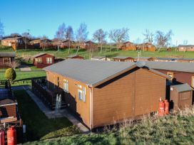 Multiple wooden cabins on grassy hills with some gas cylinders outside at The Sanctuary in Badgers Retreat Holiday Park near Catterick Garrison North Yorkshire
