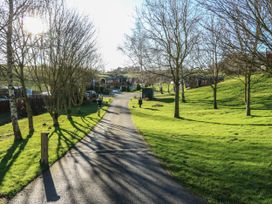 A paved pathway through a grassy area with leafless trees and wooden homes at The Sanctuary in Badgers Retreat Holiday Park near Catterick Garrison North Yorkshire